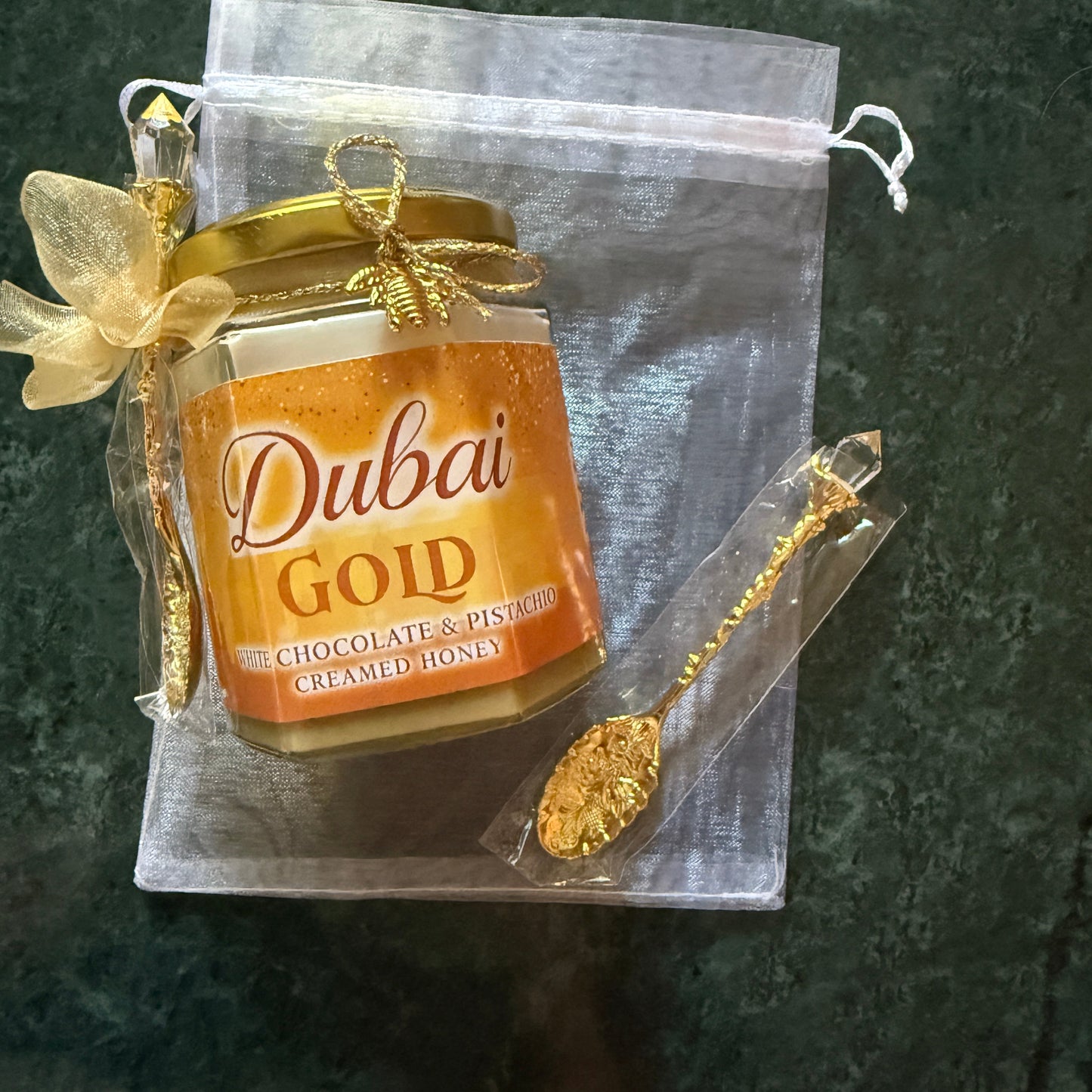 Luxury honey gift jar with gold lid, chiffon ribbon, and gold spoon on a white background – Dubai-inspired flavored honey presentation