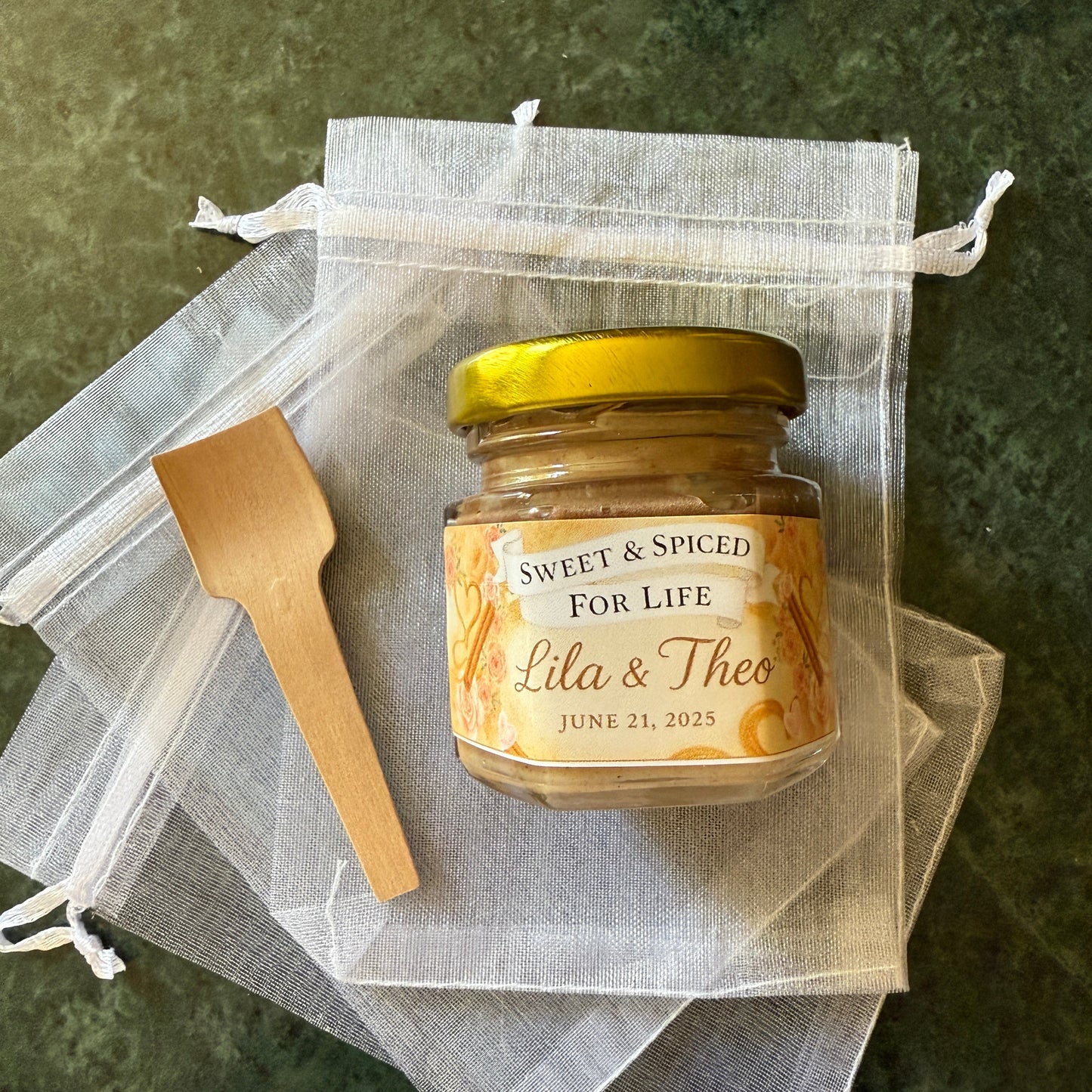 Mini honey jars with gold lids and custom labels arranged for guest wedding favors. Shelf-stable, edible gifts for bridal showers.