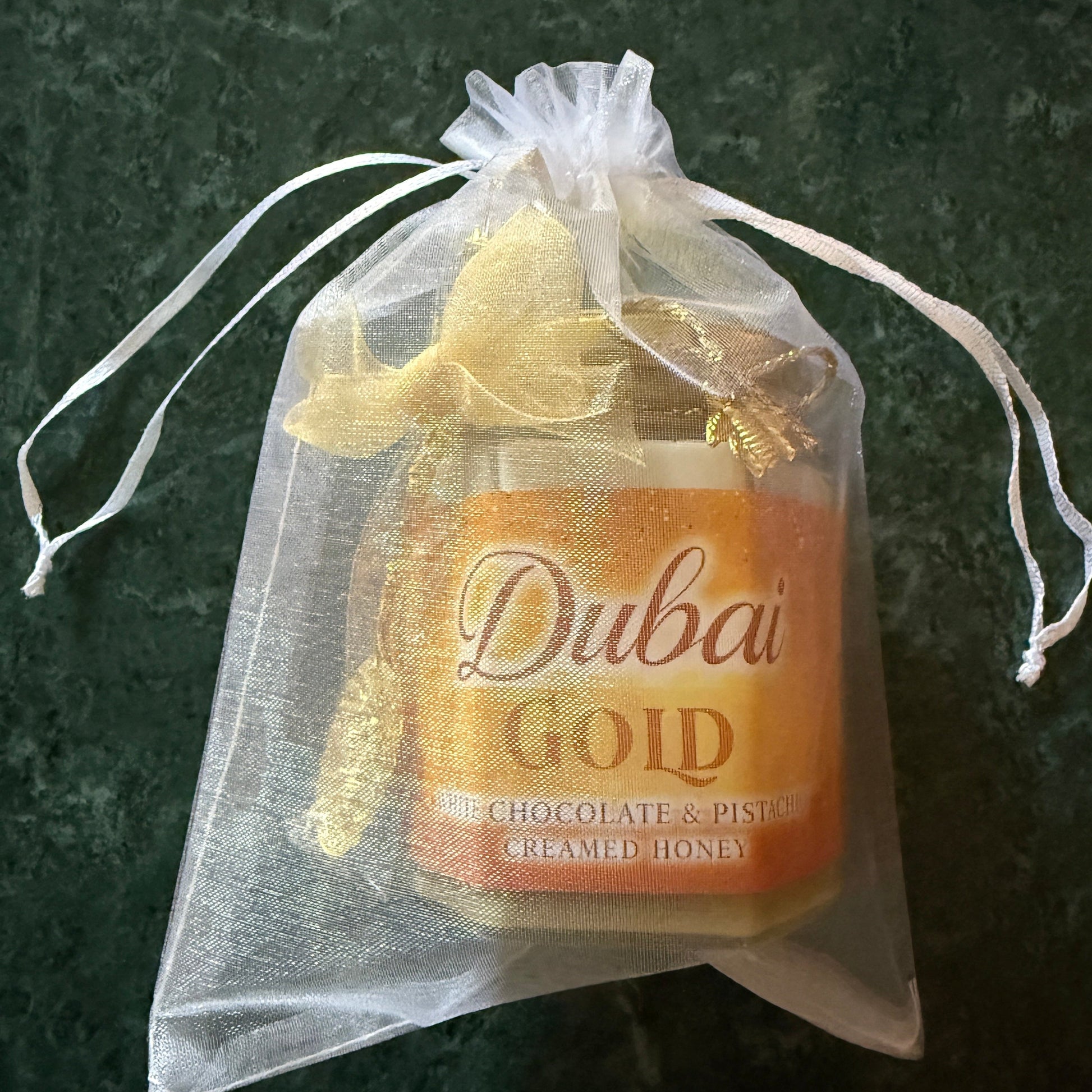 Luxury honey gift jar with gold lid, chiffon ribbon, and gold spoon on a white background – Dubai-inspired flavored honey presentation