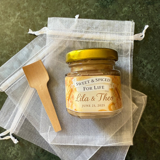 Mini honey jars with gold lids and custom labels arranged for guest wedding favors. Shelf-stable, edible gifts for bridal showers.